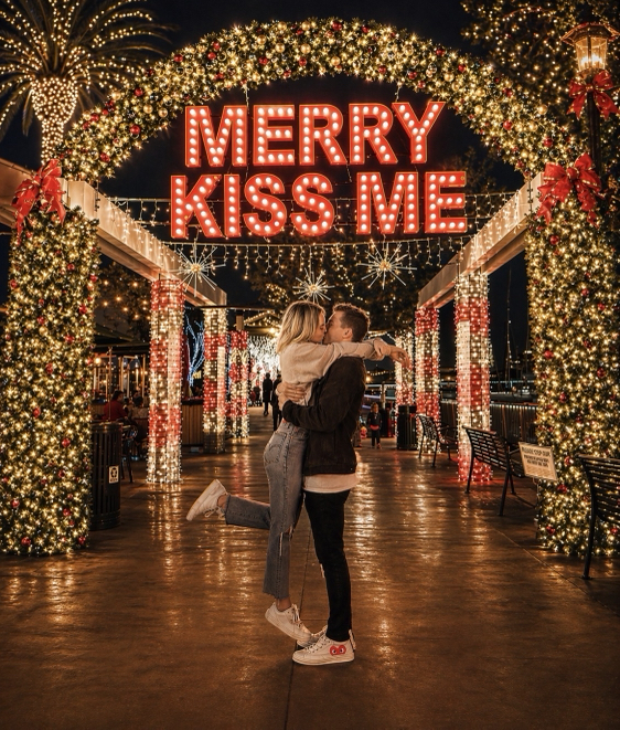 Couple kissing beneath Merry Kiss Me lights at night