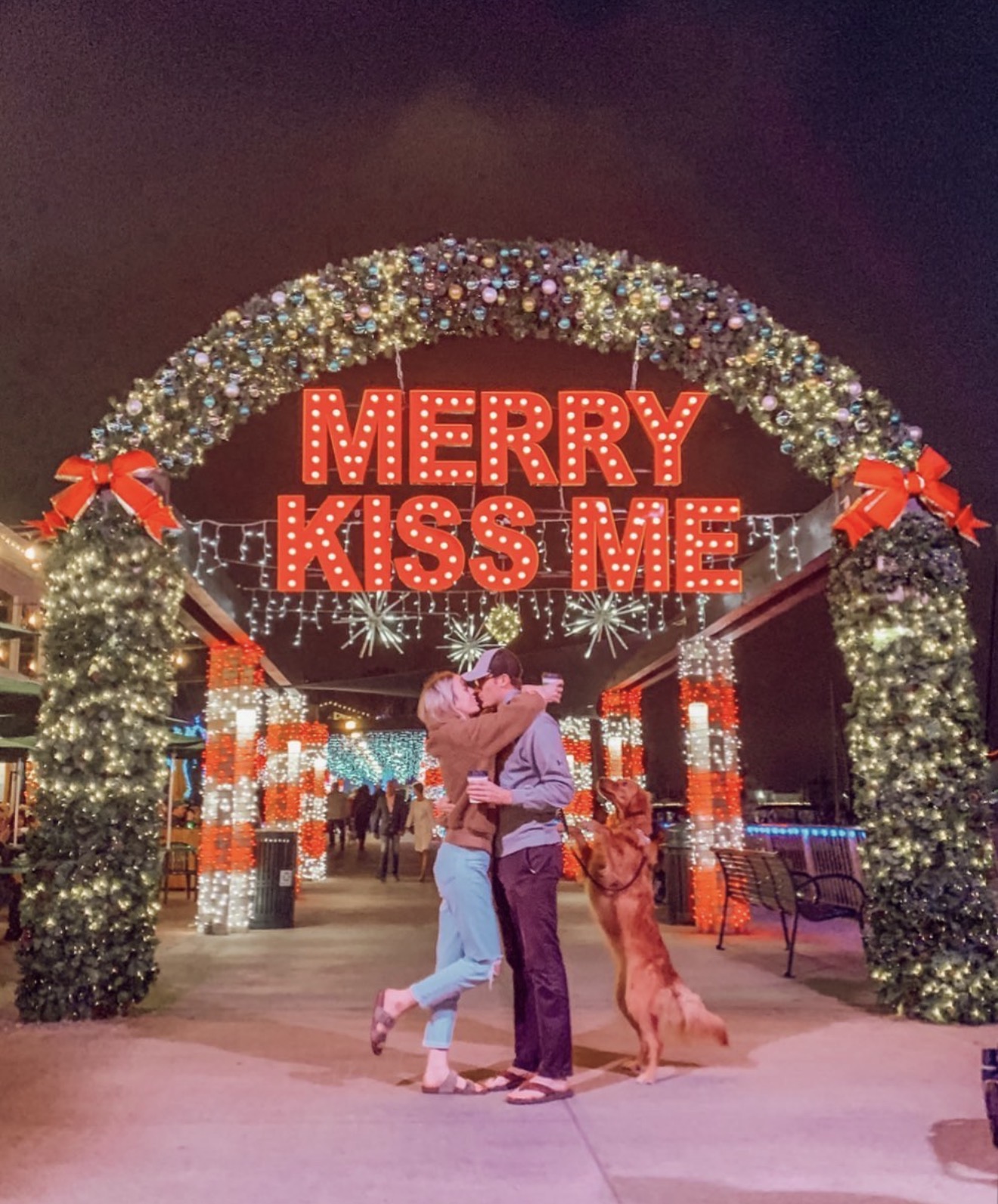 Couple and dog beneath Merry Kiss Me at night